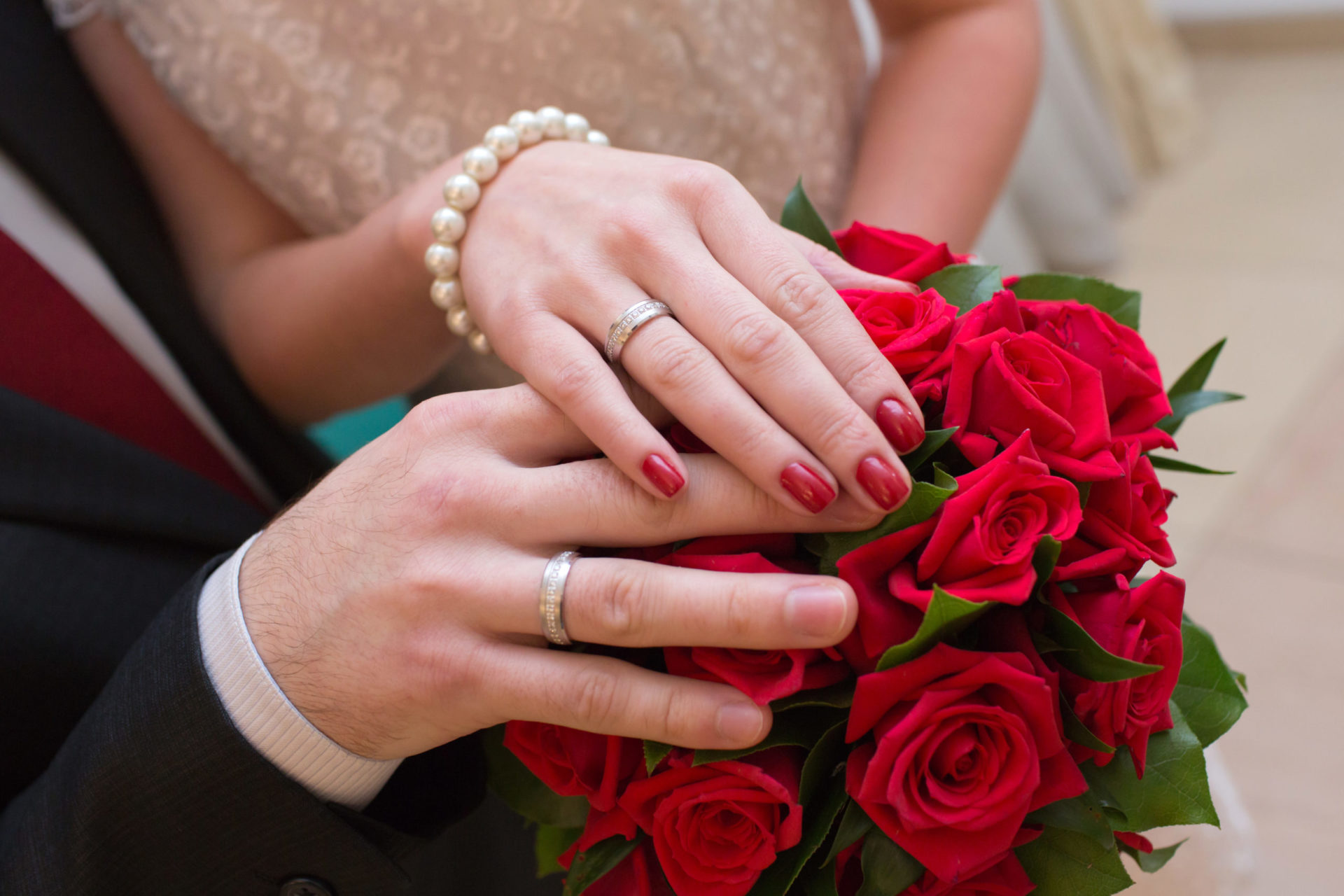 Hands of the groom and the bride with wedding rings on wedding bouquet
